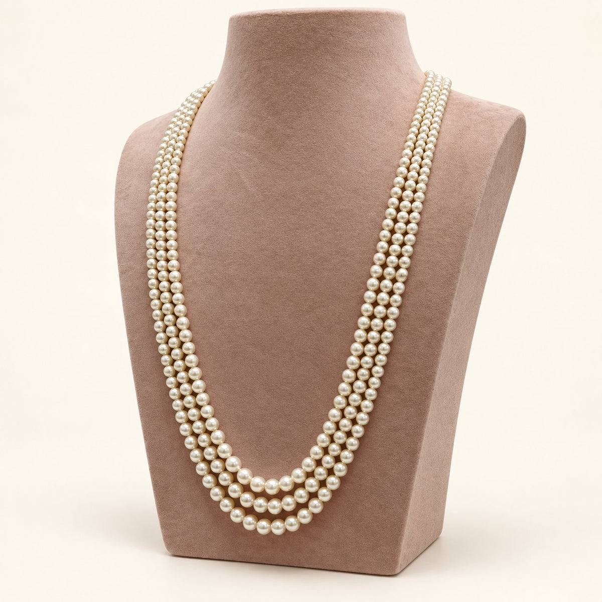 Cream triple-strand pearl-style necklace on a taupe bust – right view