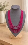 Fuchsia graduated multi-strand beaded necklace on a grey bust on an oak table